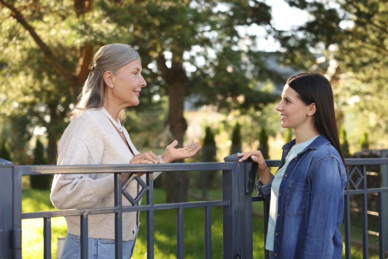 Happy women talking near fence outdoors